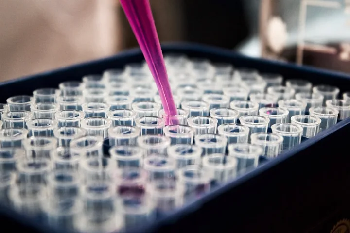 A pipette suspended over a tray of clear lab vials